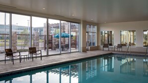 An indoor swimming pool with clear glass walls, a tiled floor, and several lounge chairs and tables. - Hyatt Place DFW (Dallas)