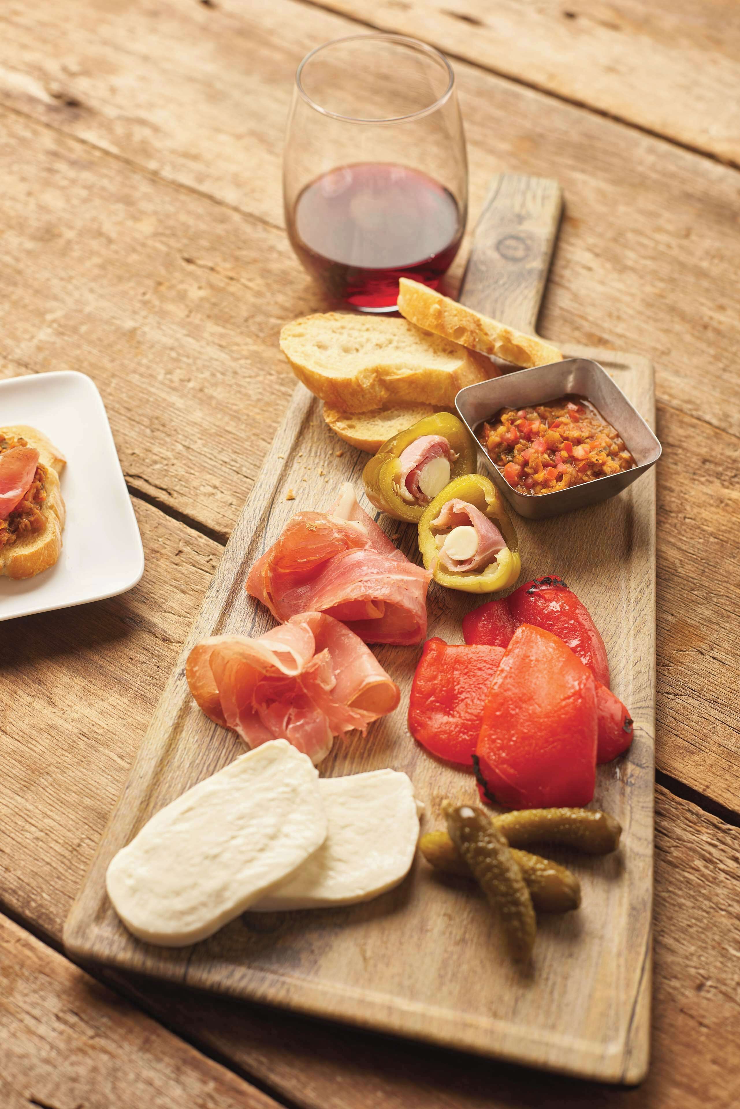 A wooden board with various foods including bread, smoked salmon, tomatoes, and pickles.