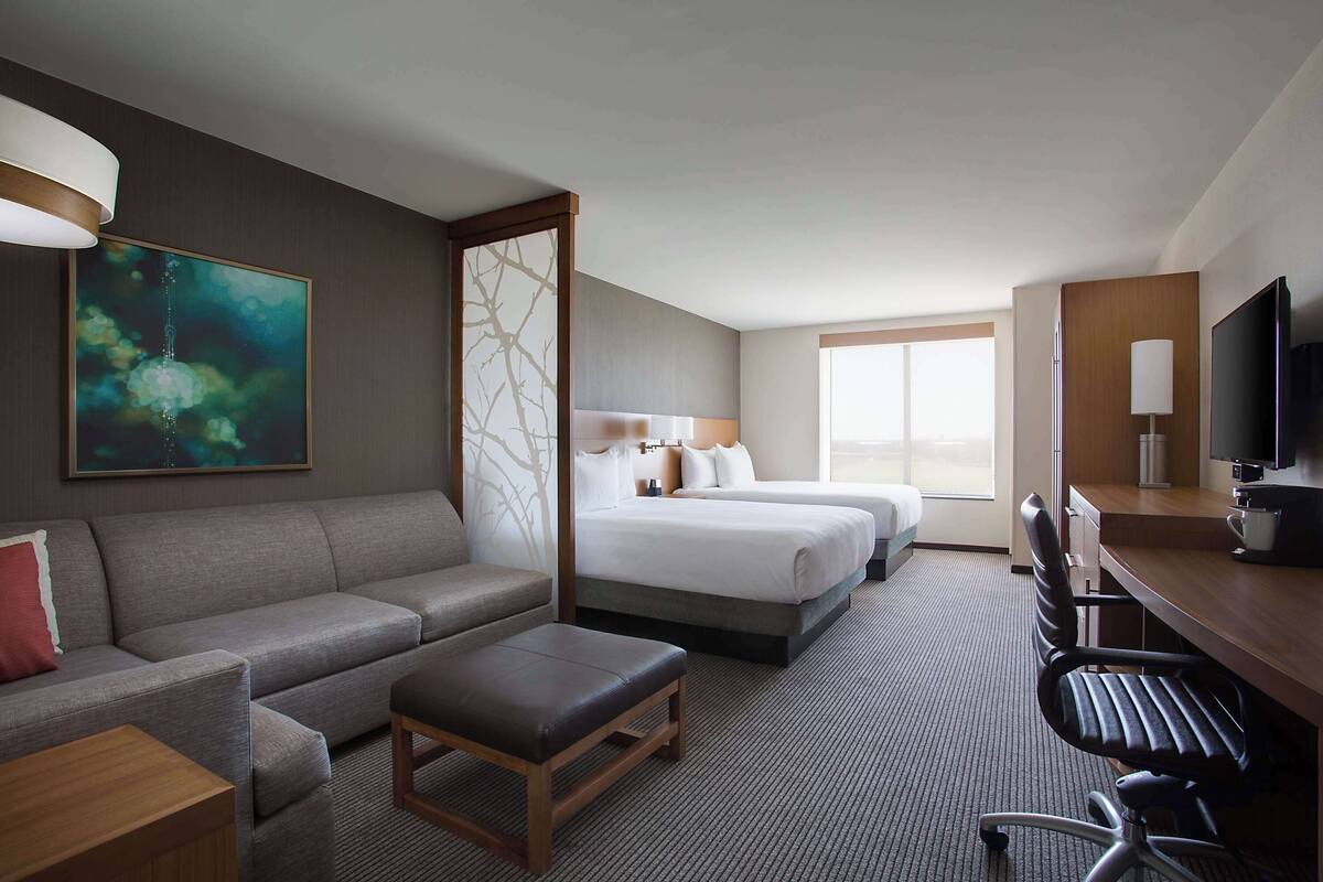 A hotel room with a sofa, two beds, a desk, a chair, and a TV.