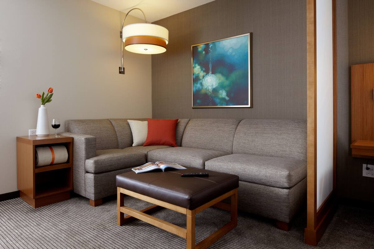 A modern living room with a sectional sofa, a wooden coffee table, a side table with a vase and wine glass, and a painting on the wall.