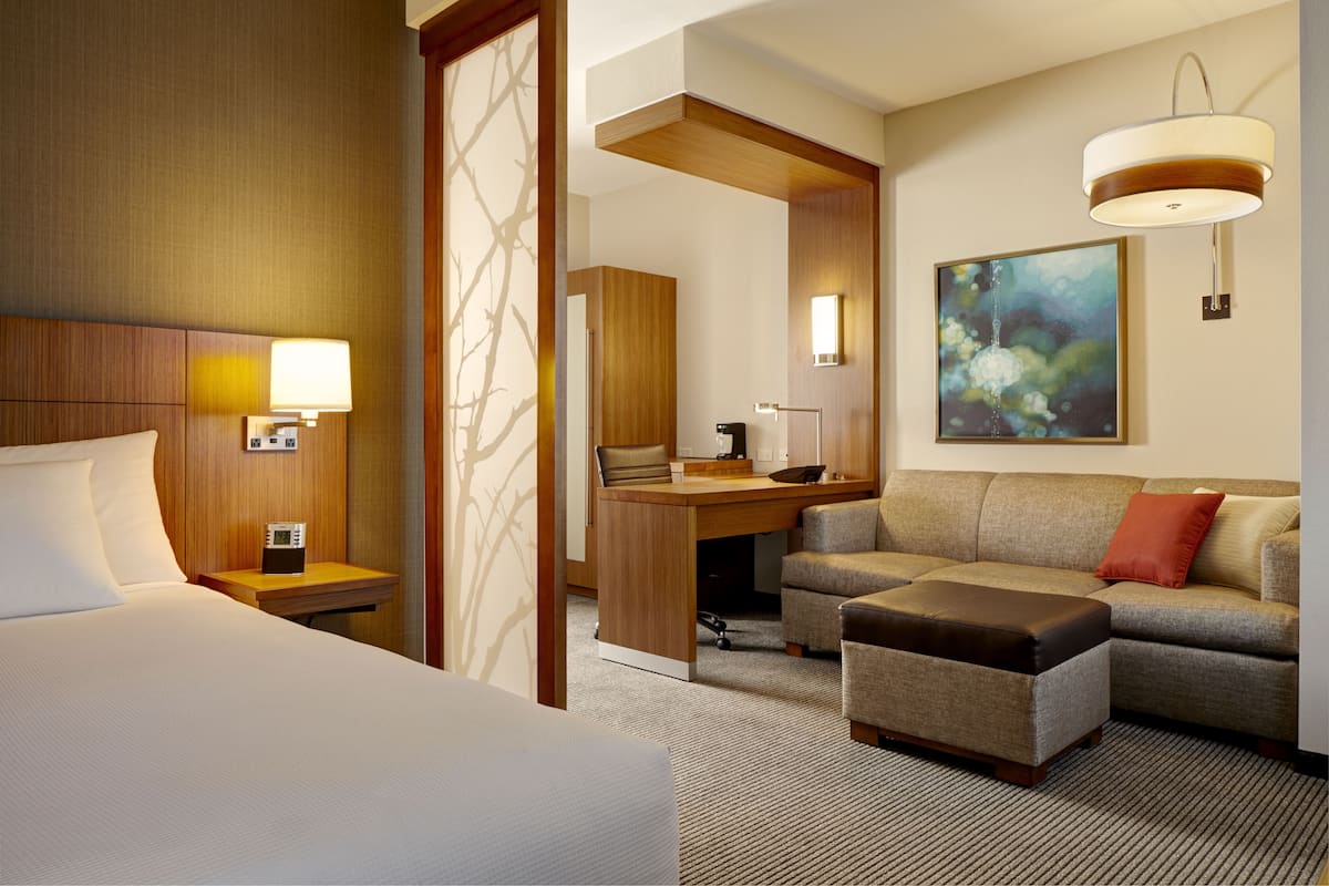 A hotel room with a bed, a desk, a sofa, and a painting on the wall.