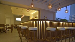 Zona de bar con taburetes de madera y una barra, una pantalla de televisión y vistas al exterior.
