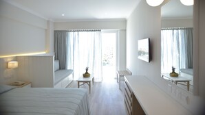 Habitación de hotel con cama, escritorio, silla, una mesita con fruta, espejo y ventana con cortinas.