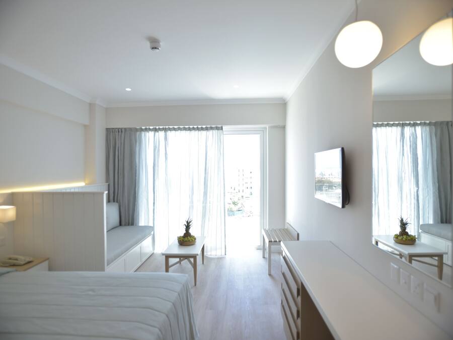 Habitación de hotel con cama, escritorio, silla, una mesita con fruta, espejo y ventana con cortinas.