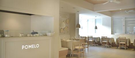 A modern kitchen with a 'POMEO' sign, wooden ceiling, and a dining area with tables and chairs.