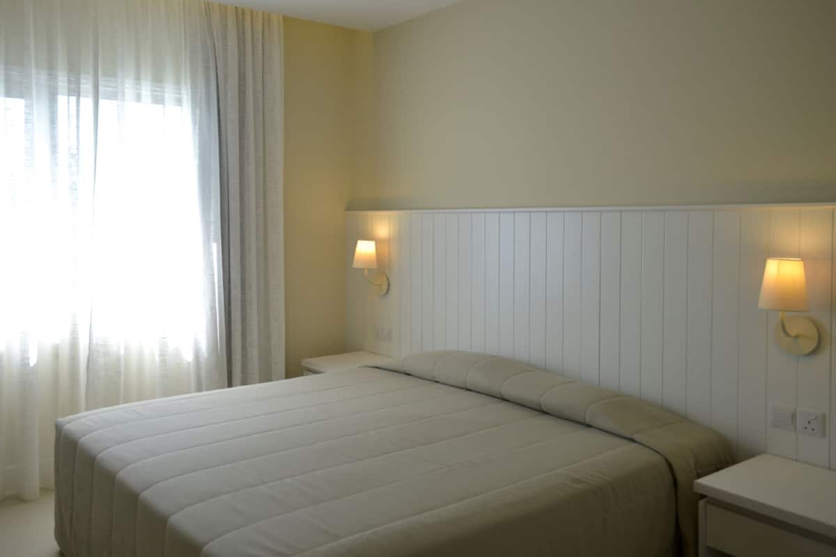 A hotel room with a bed, two bedside tables, and two wall-mounted lamps.