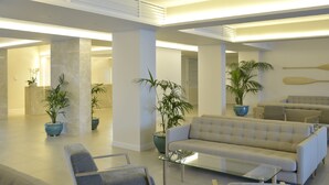 Un hall espacioso de diseño moderno, con un amplio sofá beige, una mesa de centro de vidrio y varias plantas en macetas.
