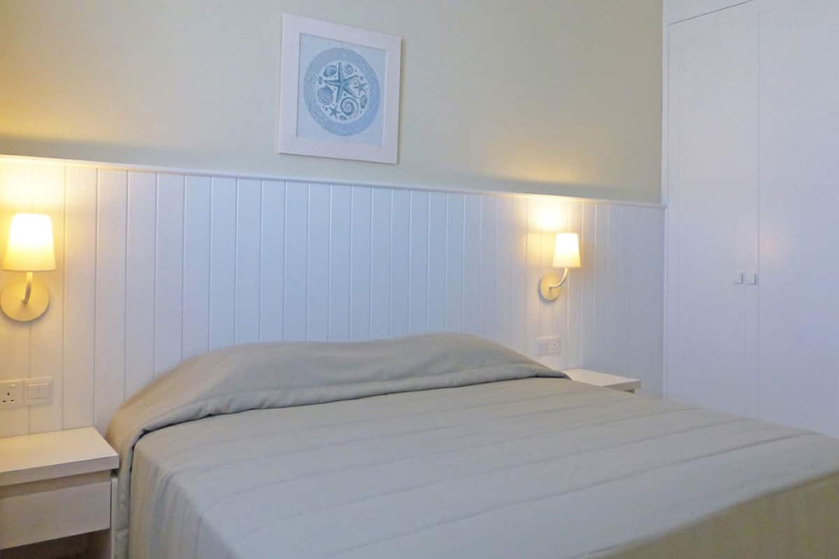 A bedroom with a bed, two bedside lamps, a wall-mounted picture, and a white wardrobe.