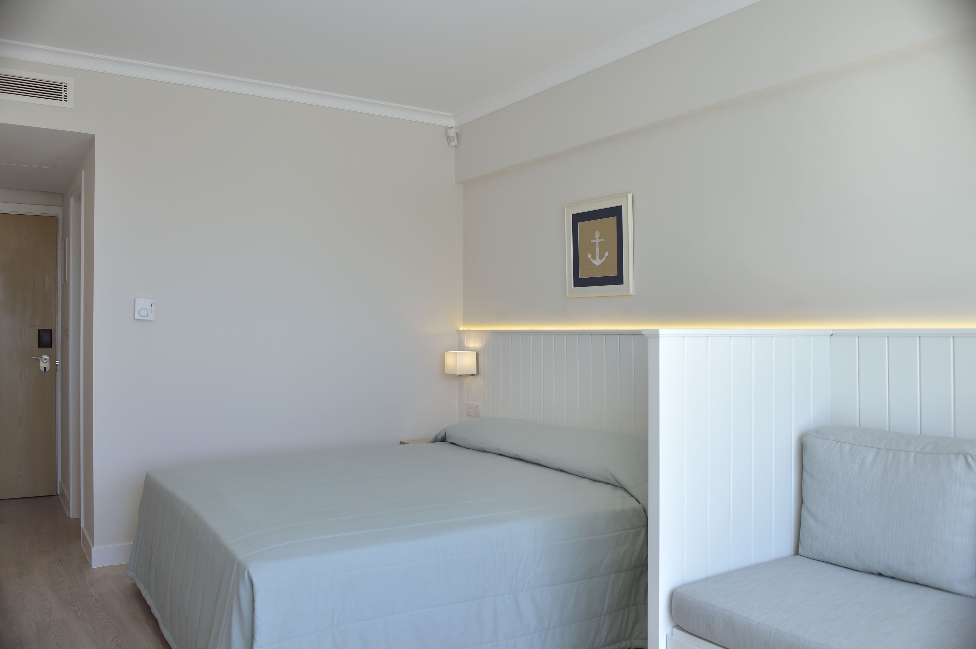 A bedroom with a bed, a bedside table, a wall-mounted light, and a framed picture.
