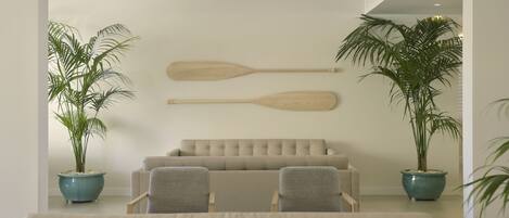 Un salon moderne avec un canapé beige, deux fauteuils et une table basse. On y trouve deux plantes en pot et deux pagaies en bois fixées au mur.
