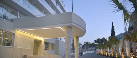 A modern hotel entrance with a covered walkway, palm trees, and a clear sky.