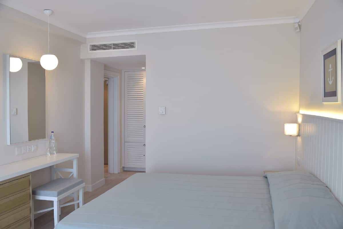 A bedroom with a bed, a bedside table, a mirror, and a wardrobe.
