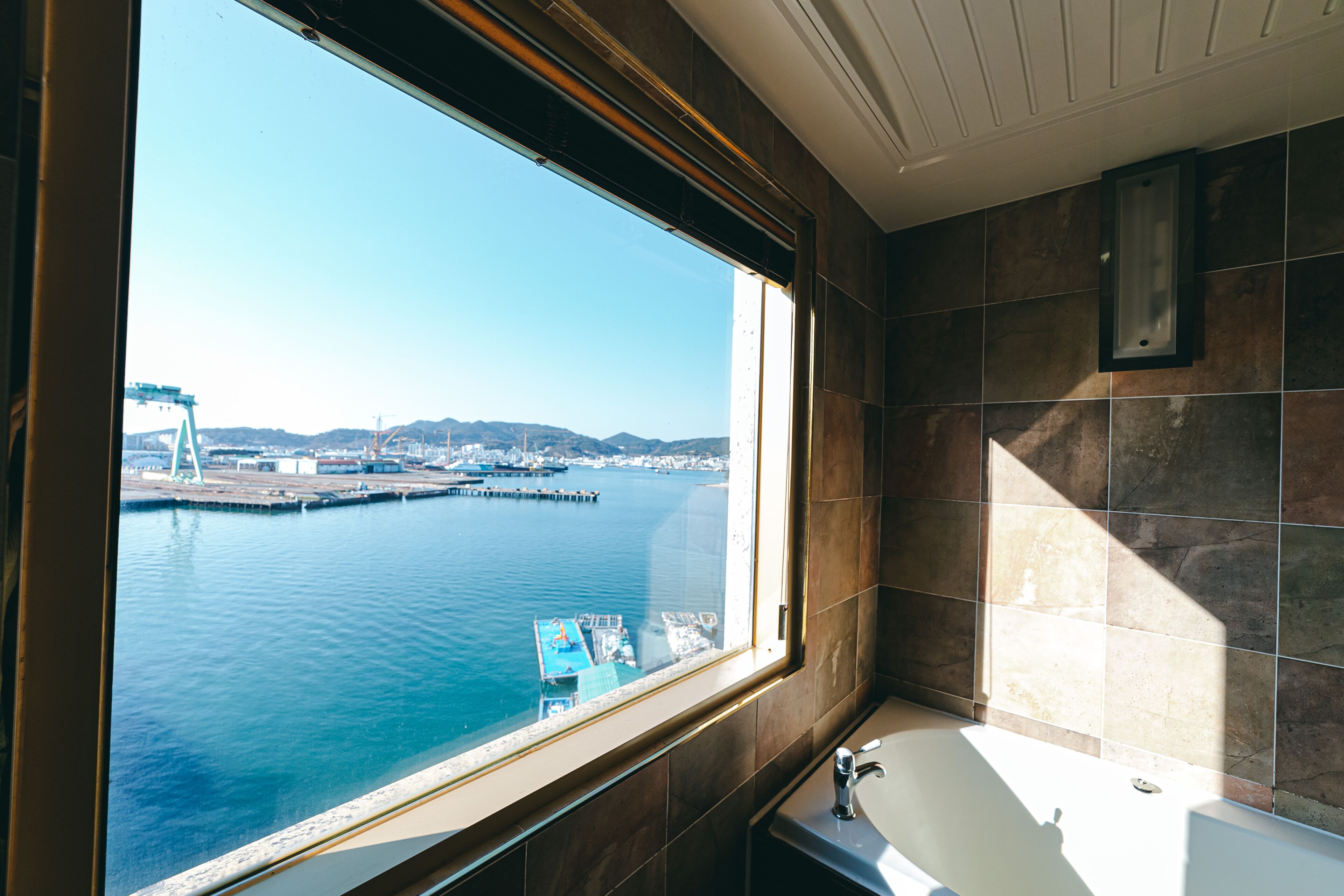 A bathroom with a large window offering a view of a harbor and a bridge.