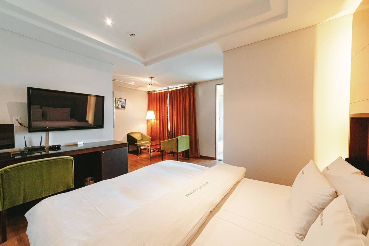 A hotel room with a large bed, a desk with a computer, a TV, and a chair.