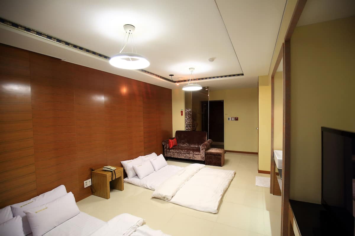 A hotel room with two beds, a sofa, a TV, and a wooden accent wall.