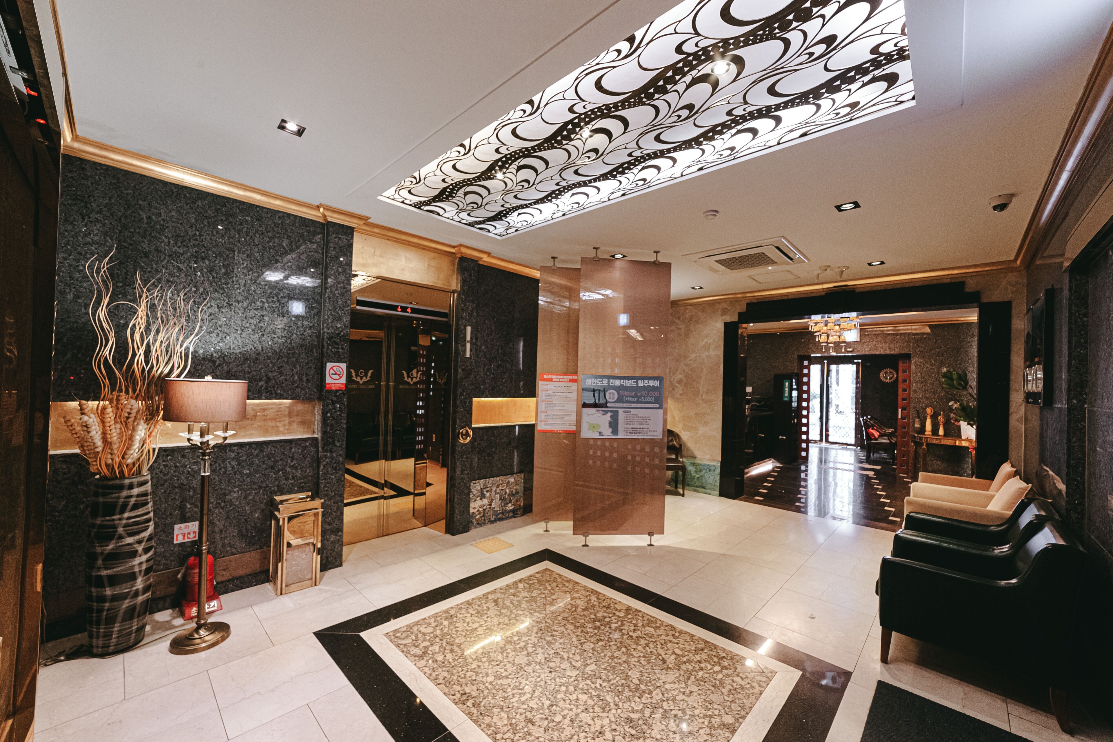 A lobby with a marble floor, a reception desk, a large vase with plants, and a chandelier.
