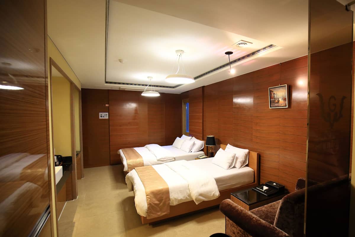 A hotel room with two beds, a small table, a chair, and a mirror.