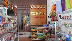 A hotel reception area with a wooden sign reading "Garden Hotel," shelves stocked with various items, and a reception desk. - Minh Anh Garden Hotel (Mui Ne)