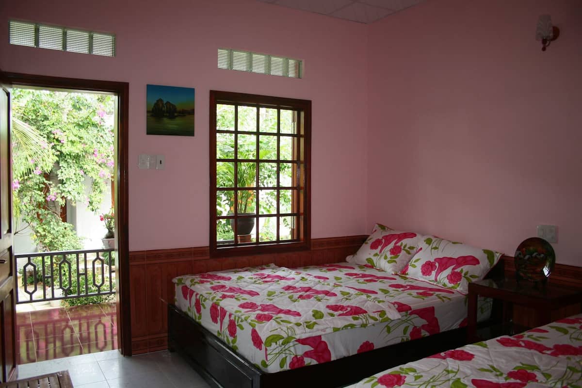 Un dormitorio con dos camas, una ventana que da a zonas verdes y una puerta que conduce a un espacio exterior.