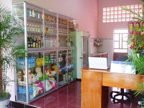 A room with a large glass display case filled with various items, a wooden desk with a laptop, and a potted plant. - Minh Anh Garden Hotel (Phan Thiet)