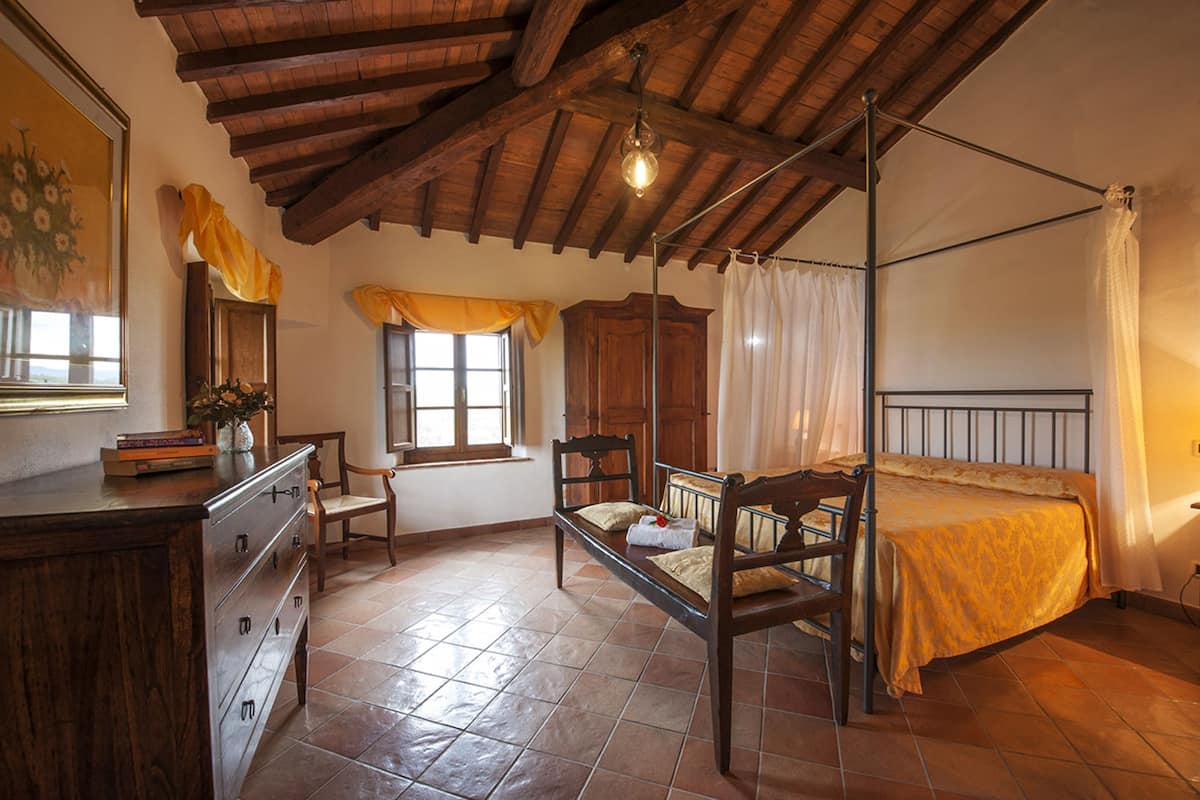 A bedroom with a four-poster bed, wooden furniture, a dresser, and a window with curtains.