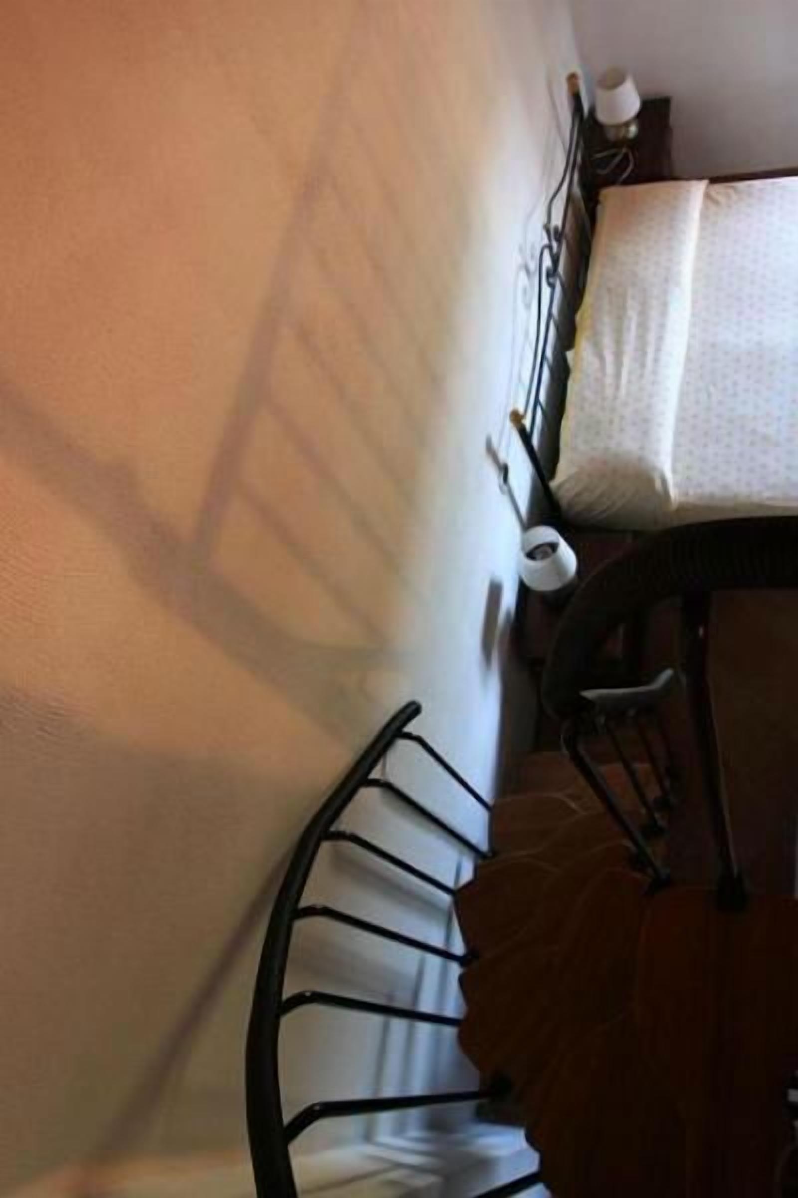 Ein Blick in einen Raum mit einem Bett, einem Nachttisch und einer an der Wand befestigten Ablage mit Kissen und Buch.