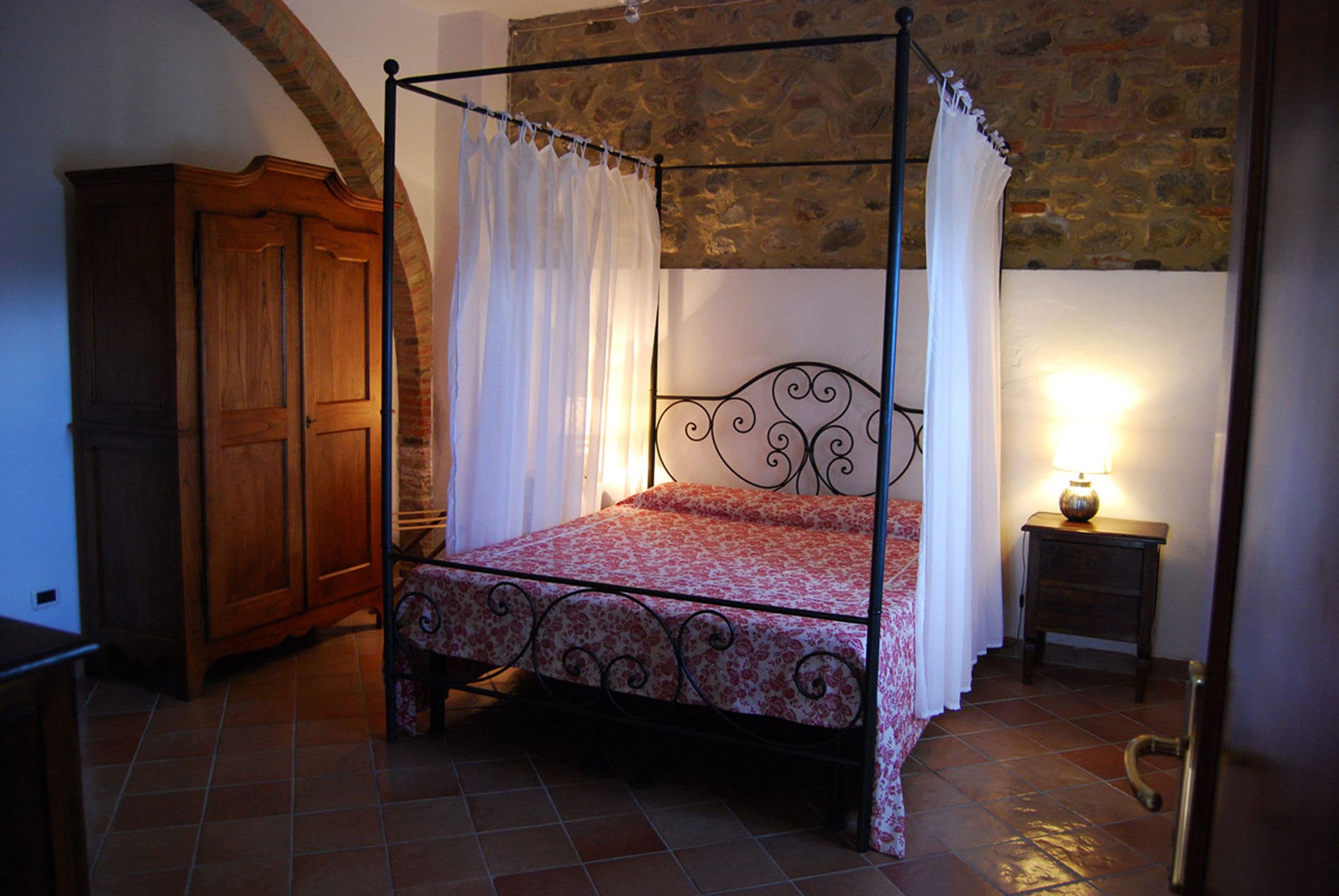 Una cama con dosel adornada con una colcha floral, un armario de madera y una pared de piedra.