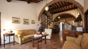 A cozy living room with a sofa, armchair, and a table with a tray of tea and cups. There is a staircase leading to an upper level, and a kitchen area is visible in the background. - Agriturismo Ragoncino (Lajatico)