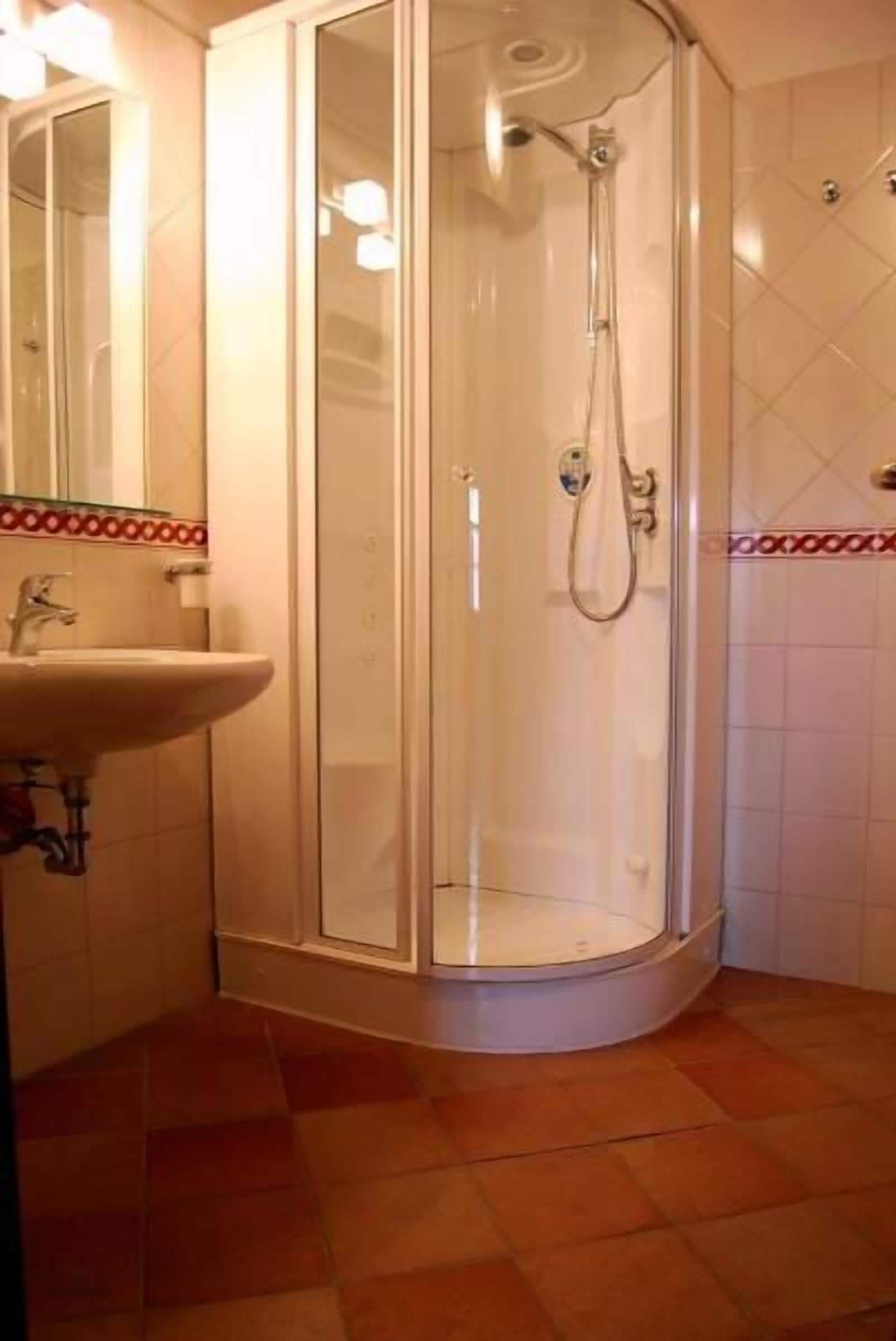 A corner bathroom with a glass shower enclosure, a sink, and a tiled floor.
