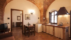 A kitchen with a brick arch, a dining area with a table and chairs, and a television in the corner. - Agriturismo Ragoncino (Lajatico)