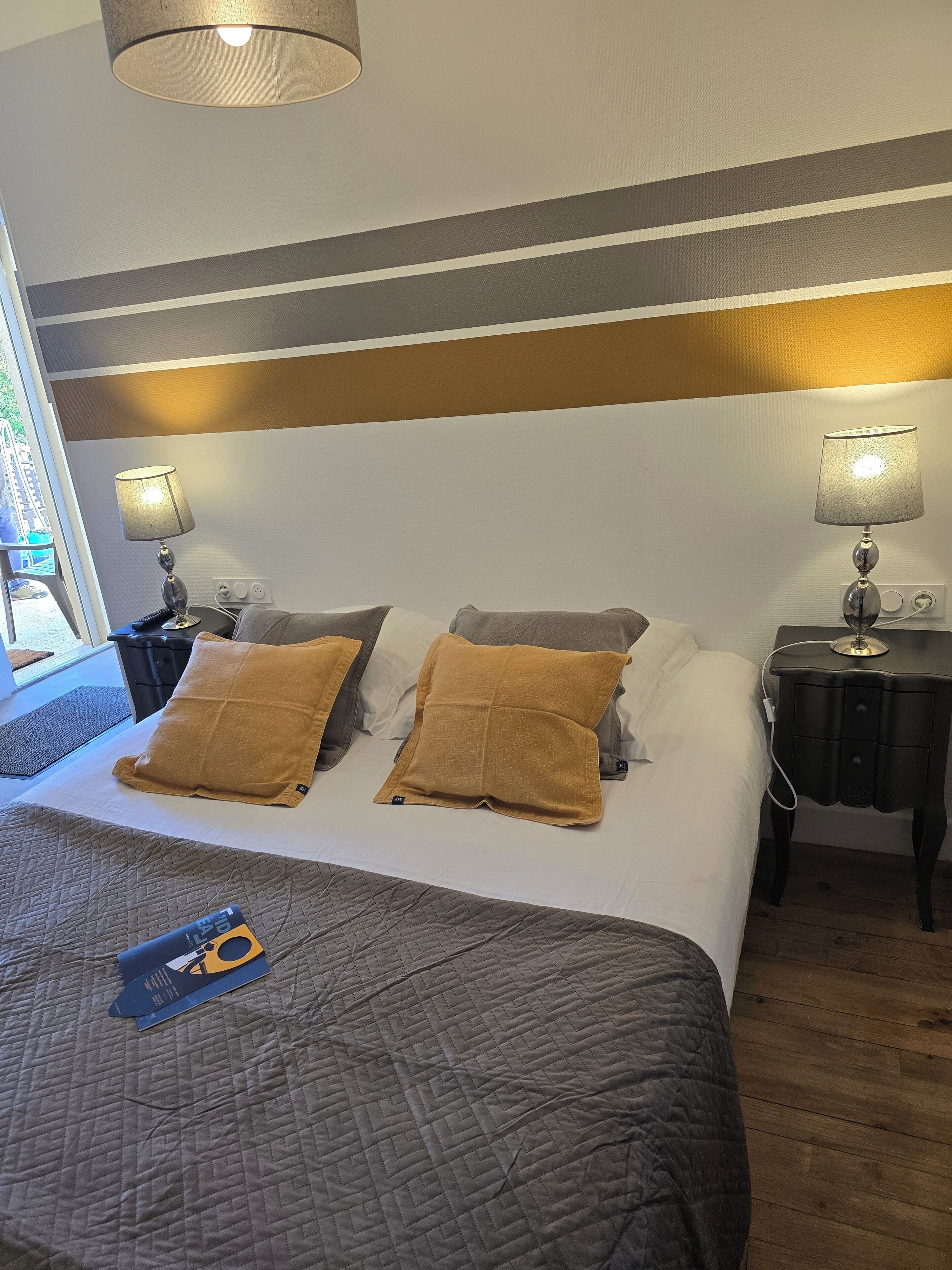A hotel room with a bed, two bedside lamps, a nightstand, and a window with a view.