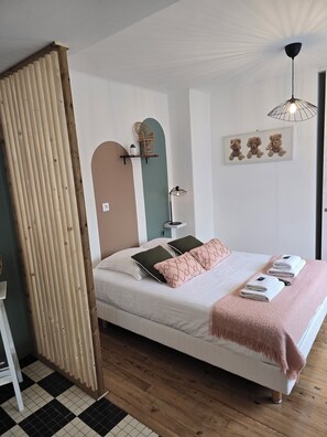 Un dormitorio con una cama, almohadas, una mesita de noche, una lámpara, un estante en la pared con objetos decorativos e iluminación en el techo.