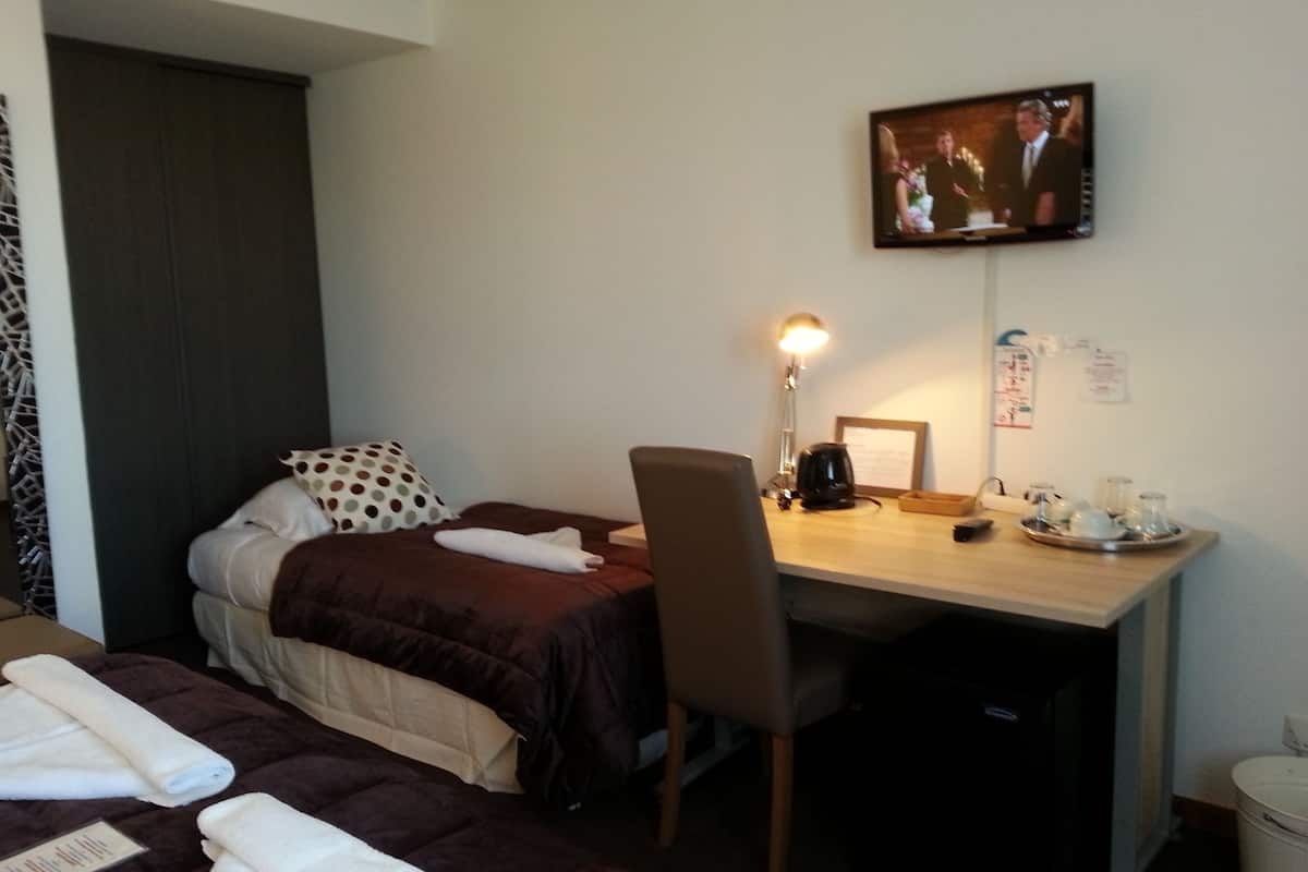 Ein Hotelzimmer mit zwei Betten, einem Schreibtisch, einem Stuhl, einem Fernseher und einer Kaffeemaschine.