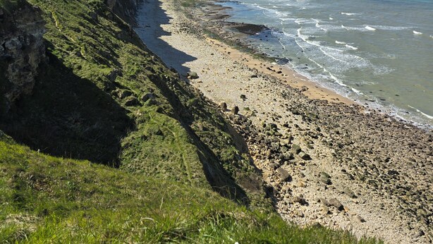 Eine Küstenlandschaft mit einer Klippe, einem Strand und dem Meer.