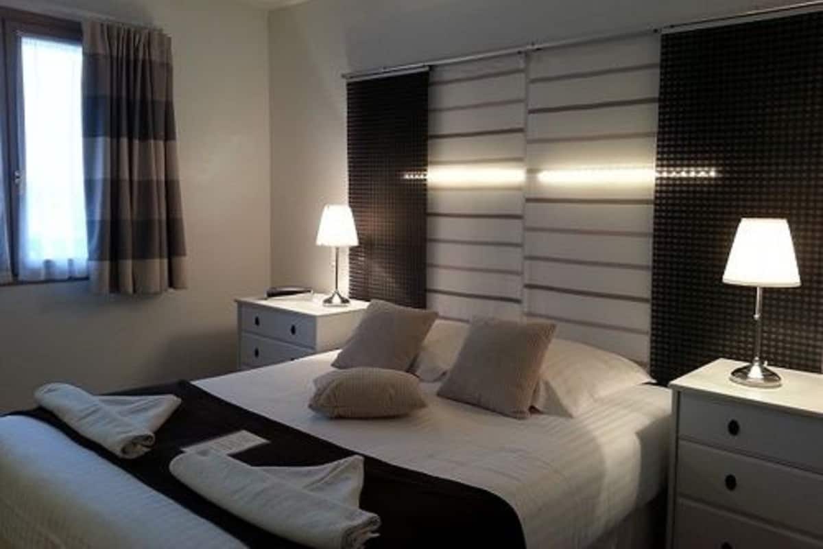 Ein Hotelzimmer mit einem Bett, zwei Nachttischen, einem Fenster mit Vorhängen und einer Wand mit einer strukturierten Wandverkleidung.