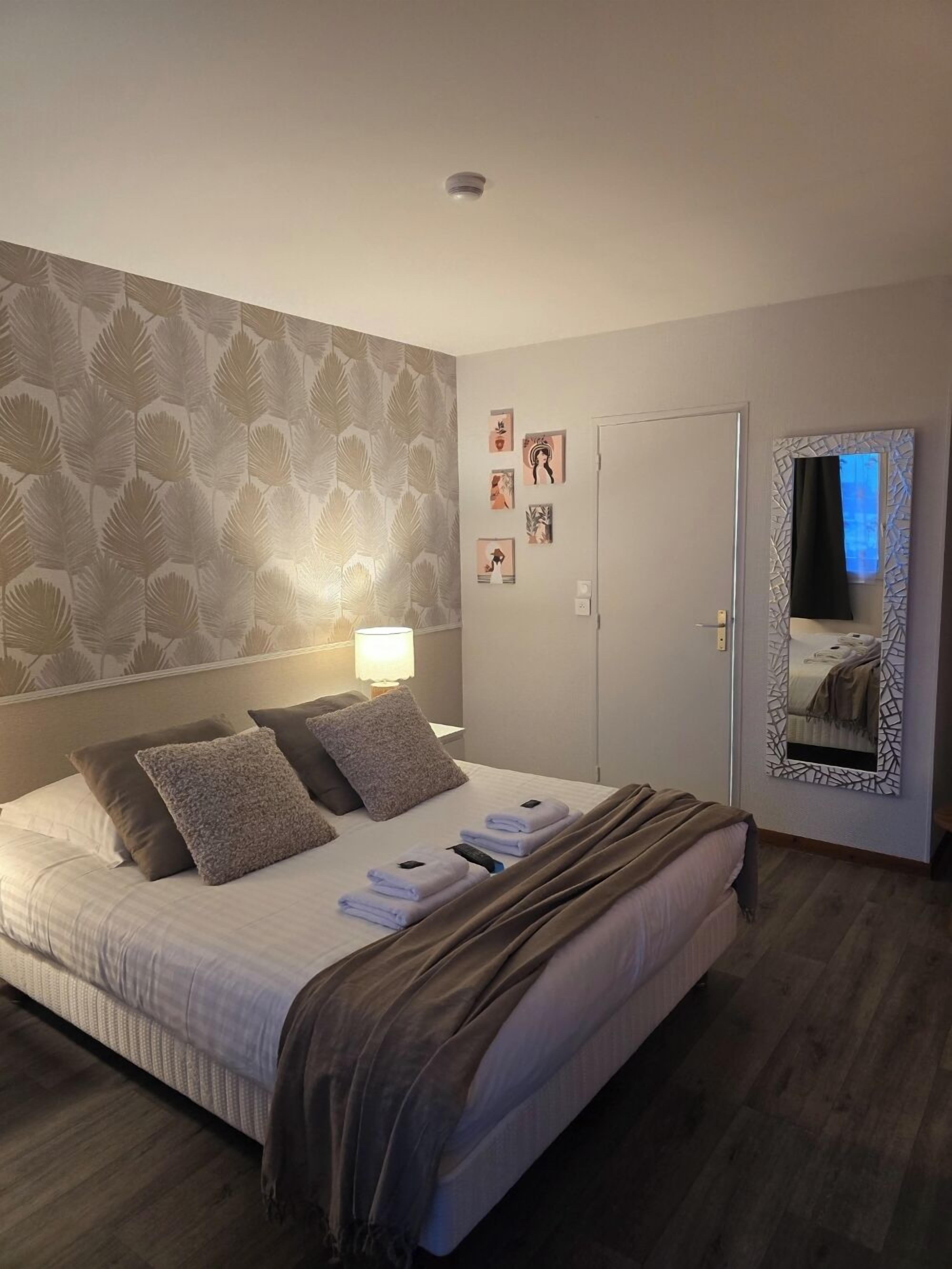 A neatly made bed with pillows and a blanket, a bedside lamp, a door, and a mirror on the wall.