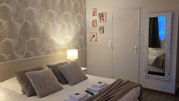 A neatly made bed with pillows and a blanket, a bedside lamp, a door, and a mirror on the wall.