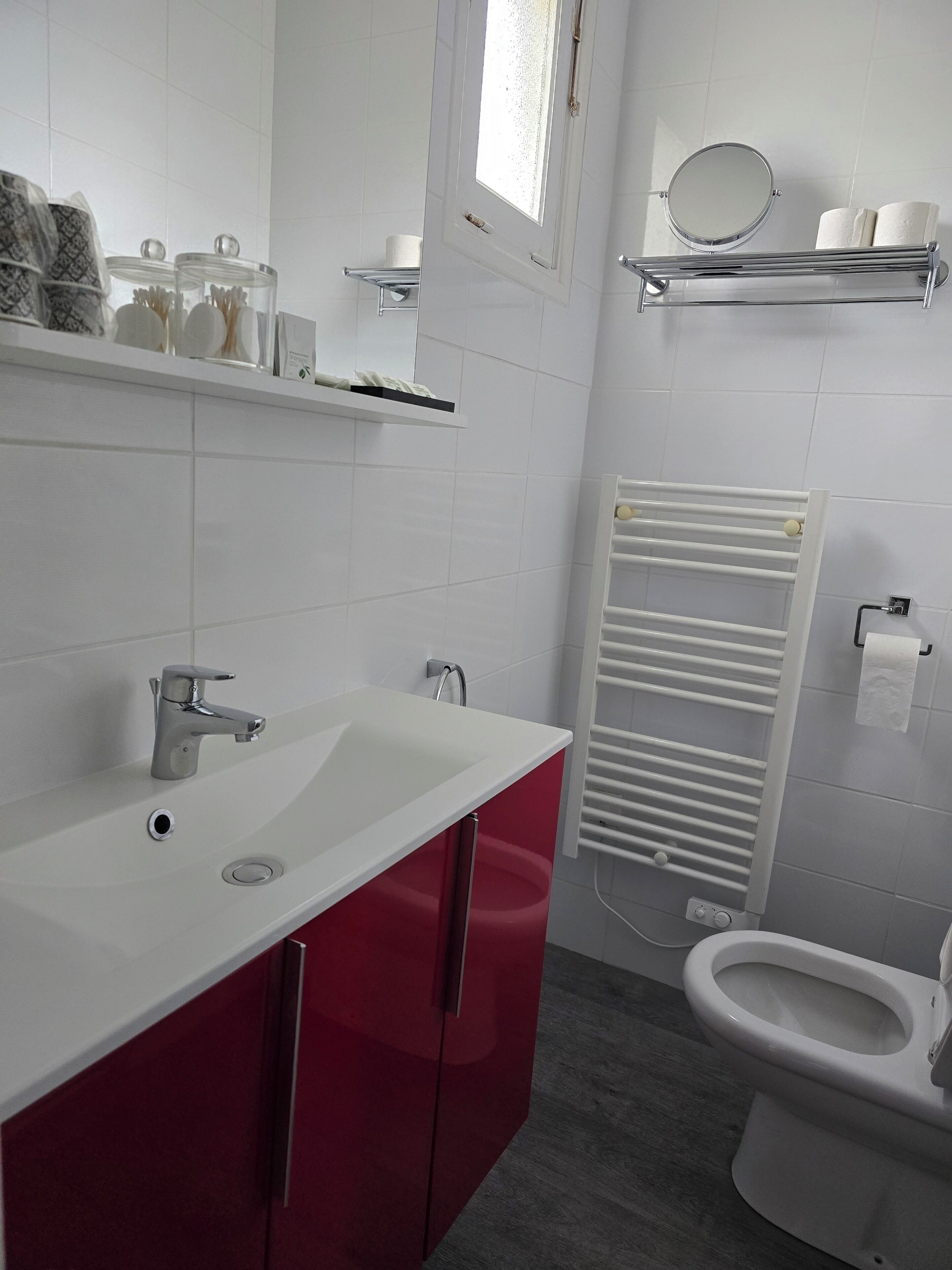A modern bathroom with a white sink, red cabinets, a white toilet, and a towel rack.