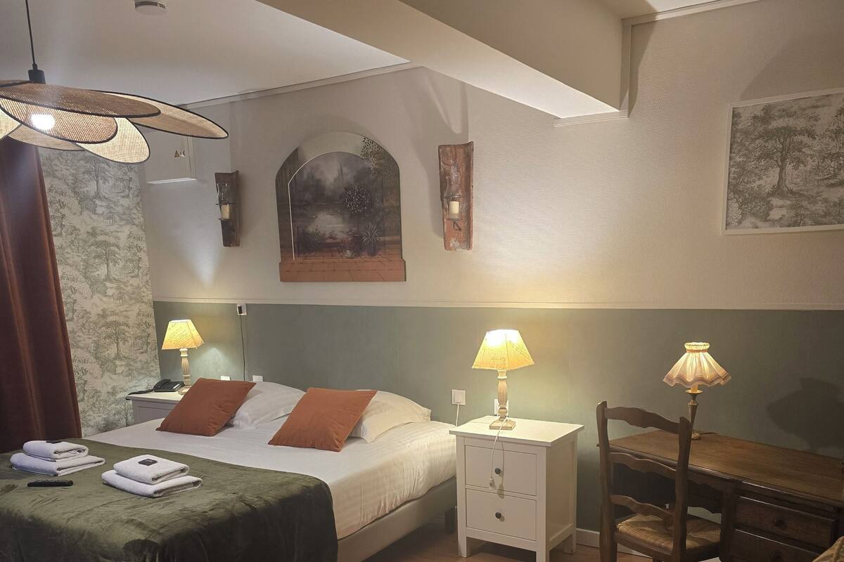 Ein Hotelzimmer mit einem Bett, zwei Nachttischen mit Lampen, einem Sessel, einem Schreibtisch und einem Wandbild.