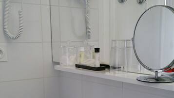 A bathroom with a white sink, a mirror, a hairdryer, and a shower.