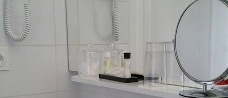A bathroom with a white sink, a mirror, a hairdryer, and a shower.