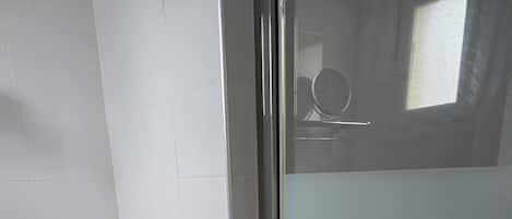 A bathroom with a toilet, a trash bin, and a glass shower enclosure.