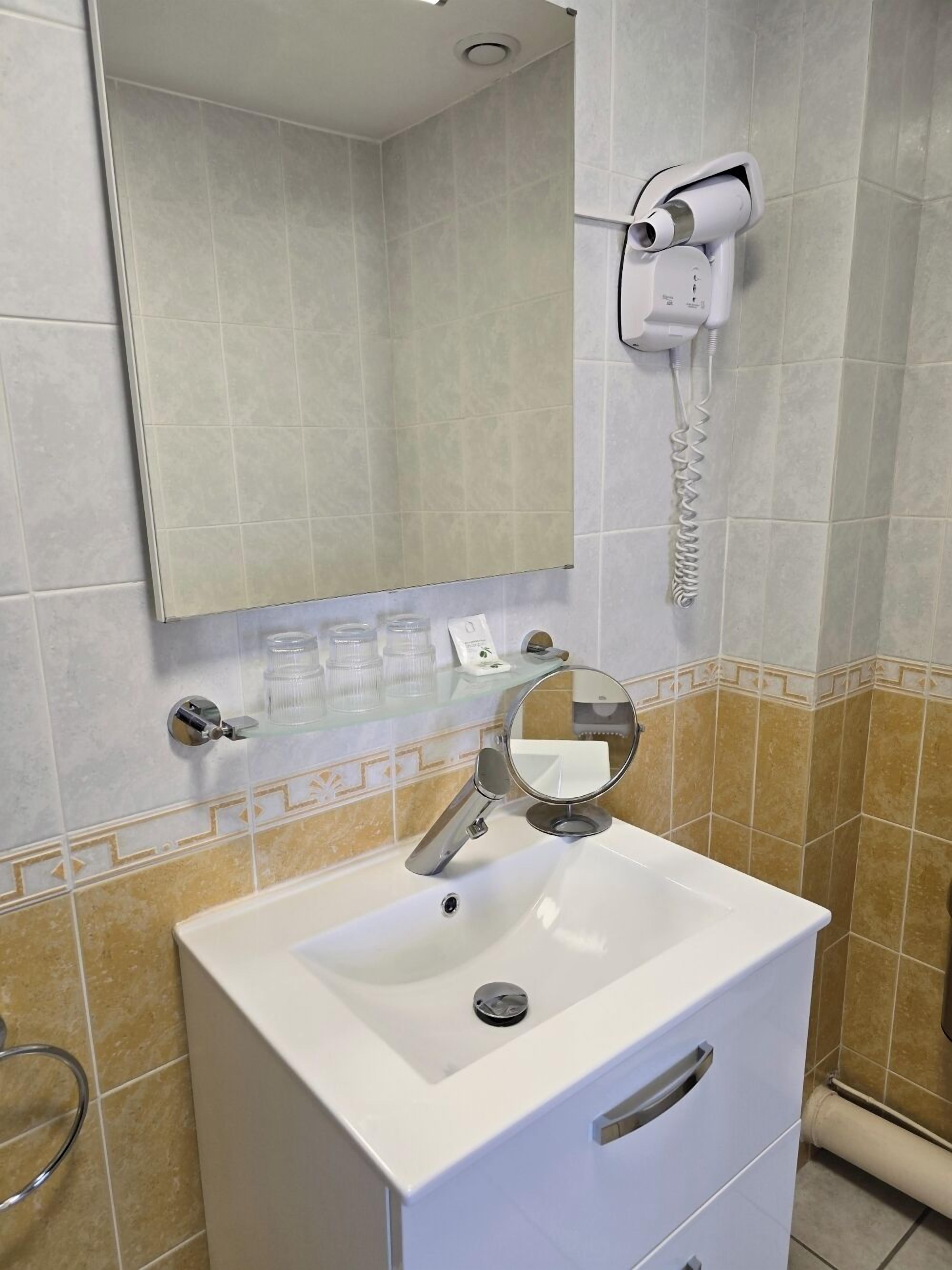 Une salle de bain avec un lavabo blanc, un miroir, un porte-serviettes et un sèche-cheveux fixé au mur.