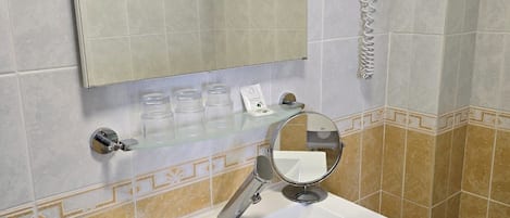 Un baño con lavamanos blanco, un espejo, toallero y un secador de pelo montado en la pared.