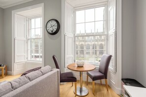 A room with a grey sofa, two chairs, a round wooden table, and a clock on the wall. - Destiny Scotland - Princes St Residence (Edinburgh)