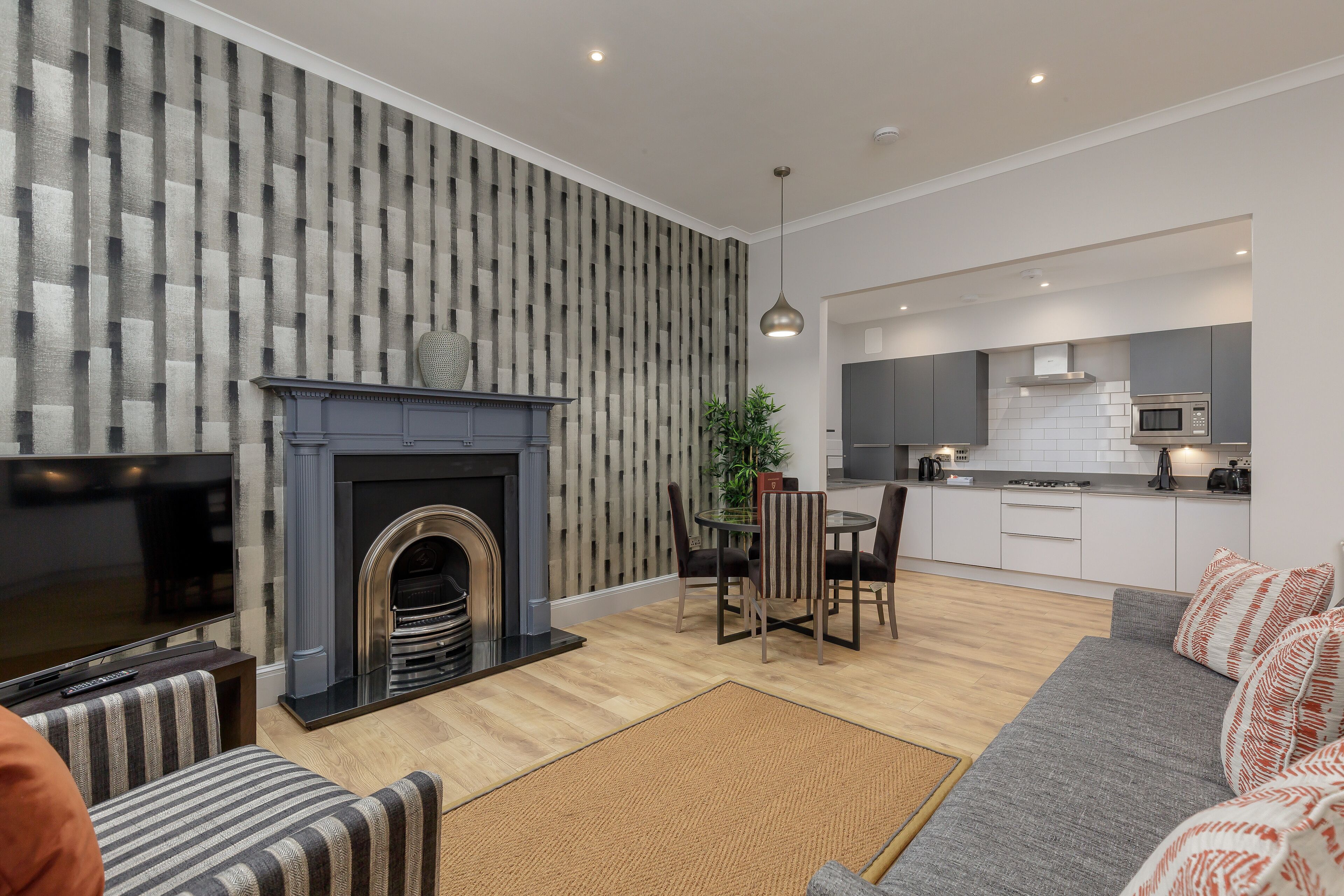 A modern living room with a fireplace, a dining area, and a kitchen with white cabinets and a microwave.