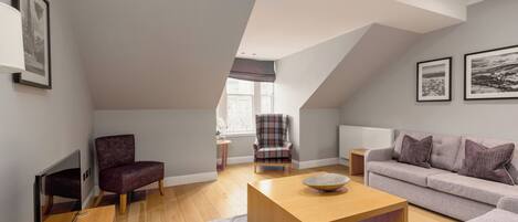 A modern living room with a wooden coffee table, a grey sofa, and a plaid armchair.