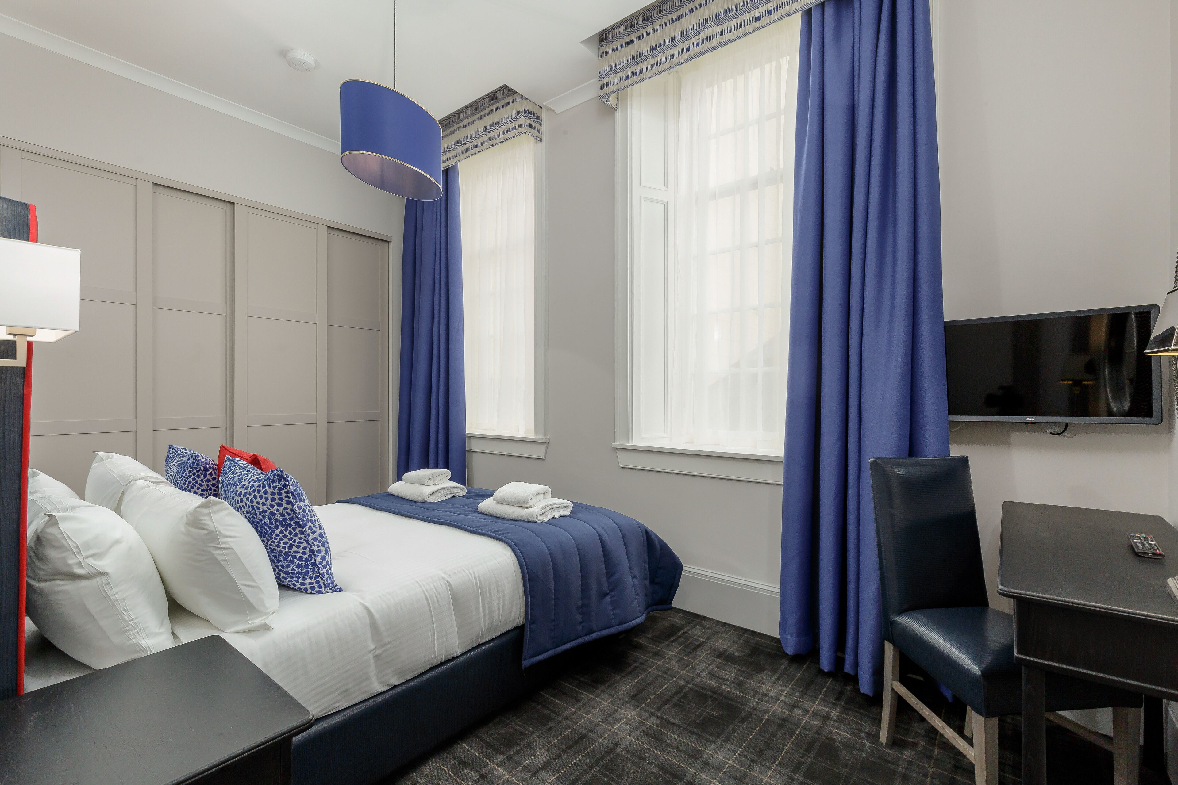 A hotel room with a bed, a desk, a chair, a TV, and a window with curtains.