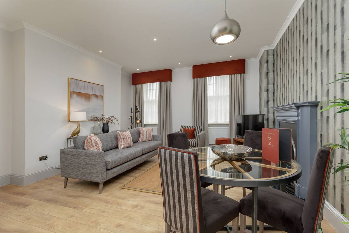 A modern living room with a grey sofa, striped chairs, a glass coffee table, and a fireplace.