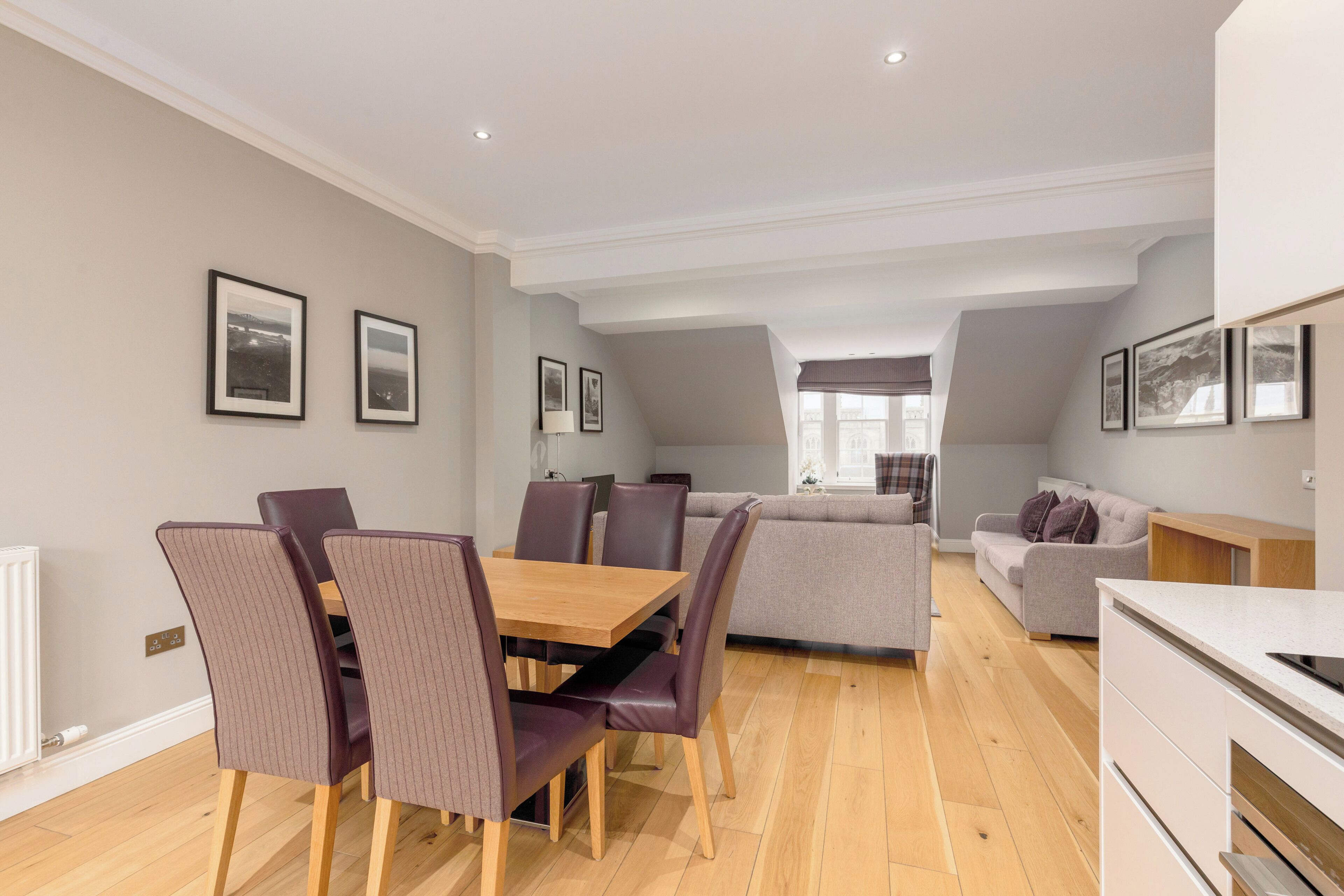 A modern living room with a dining area, grey sofas, and a wooden dining table.
